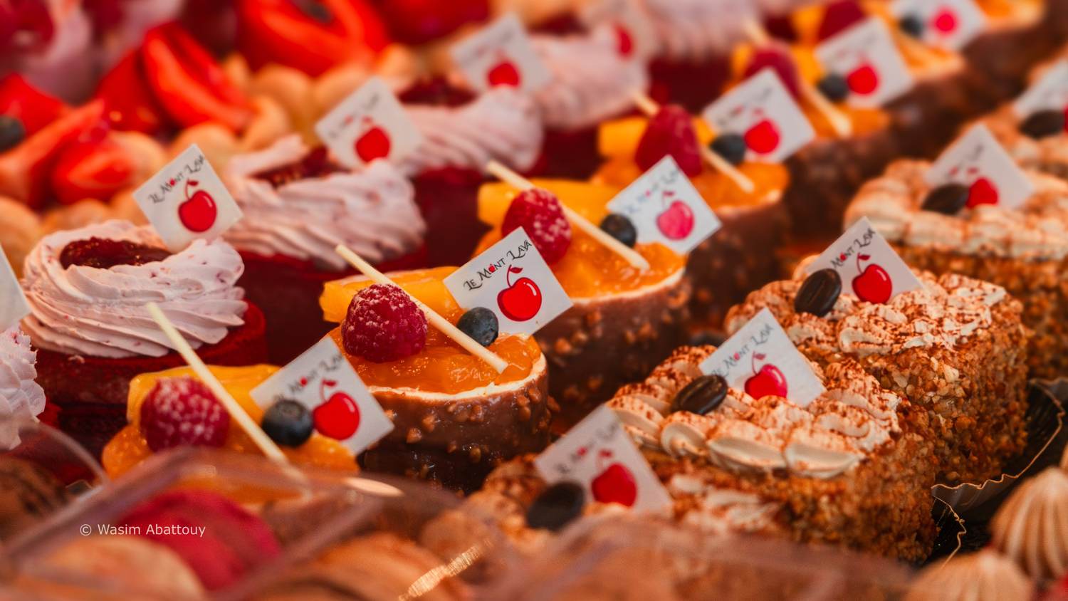 Rows of small pastries topped with raspberries and cherry flags
