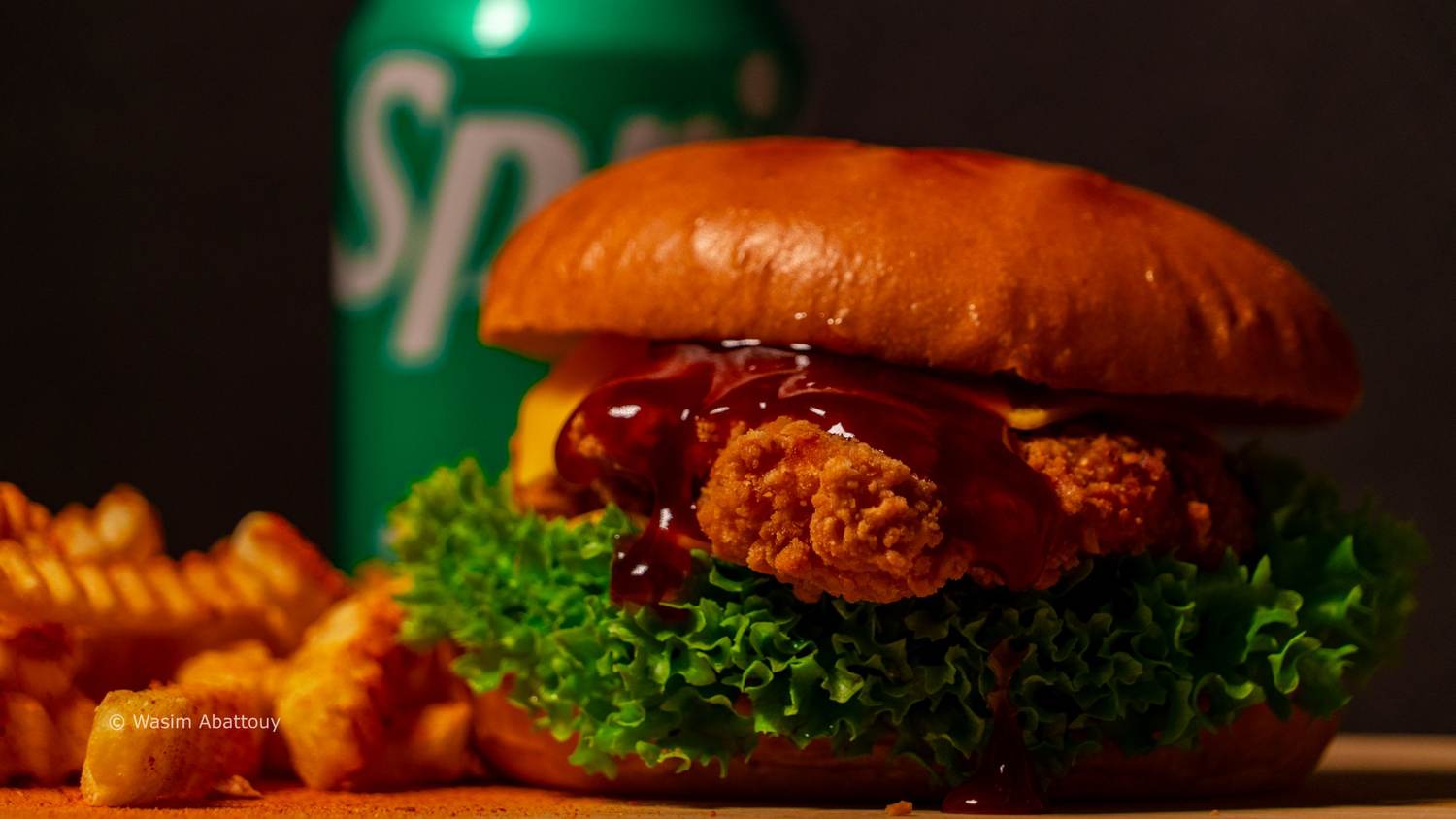 Crispy chicken burger with barbecue sauce in front of a green soda can