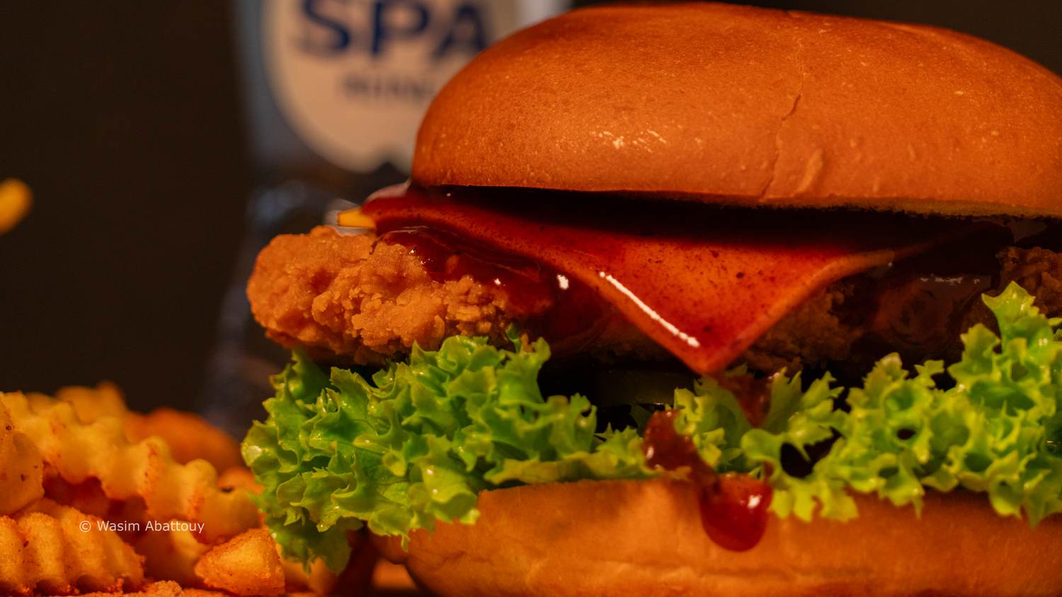 Chicken burger with melted cheese and red sauce, fries in the foreground