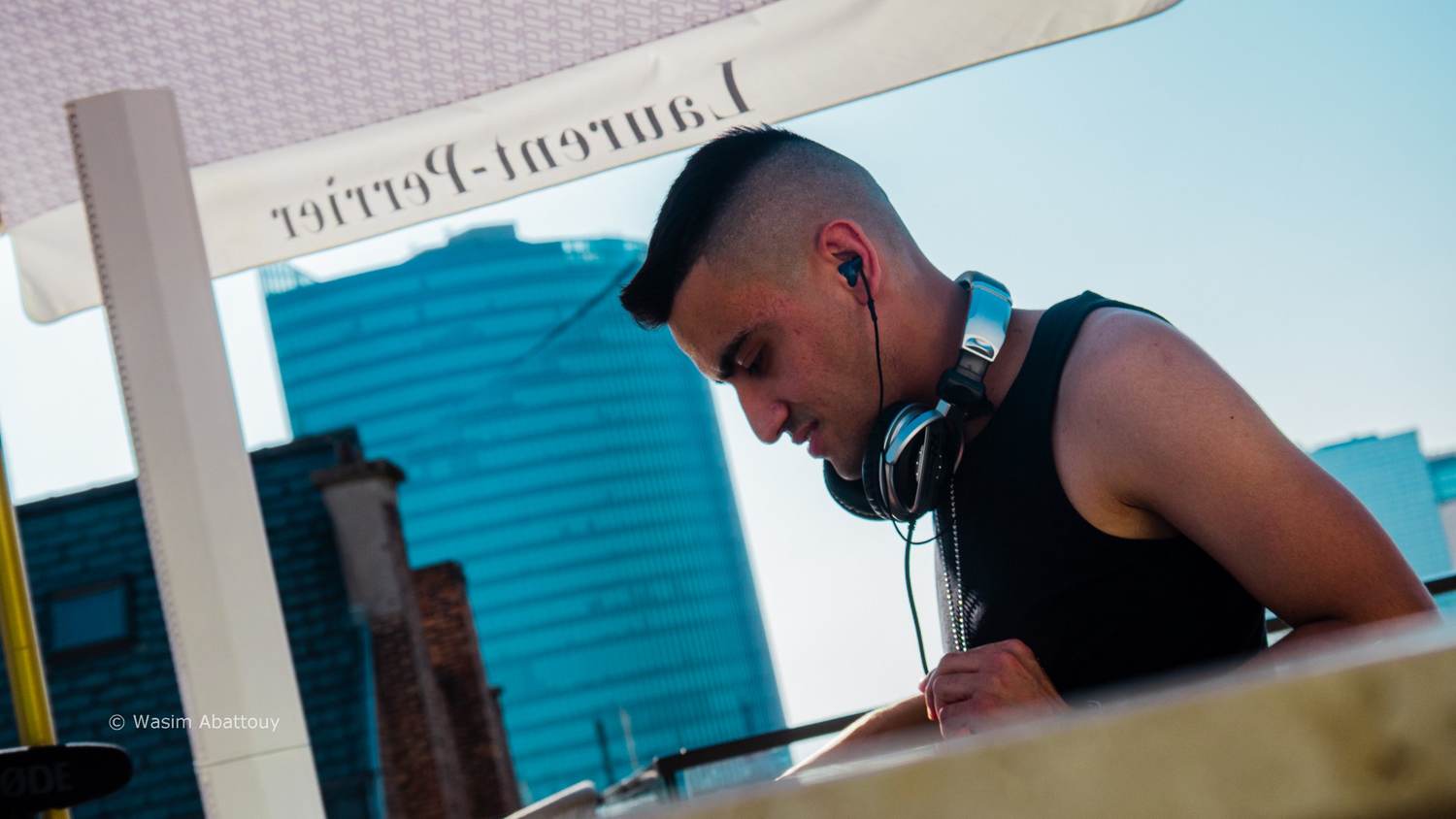 DJ looking down at the decks under a Laurent-Perrier parasol, a glass tower behind him