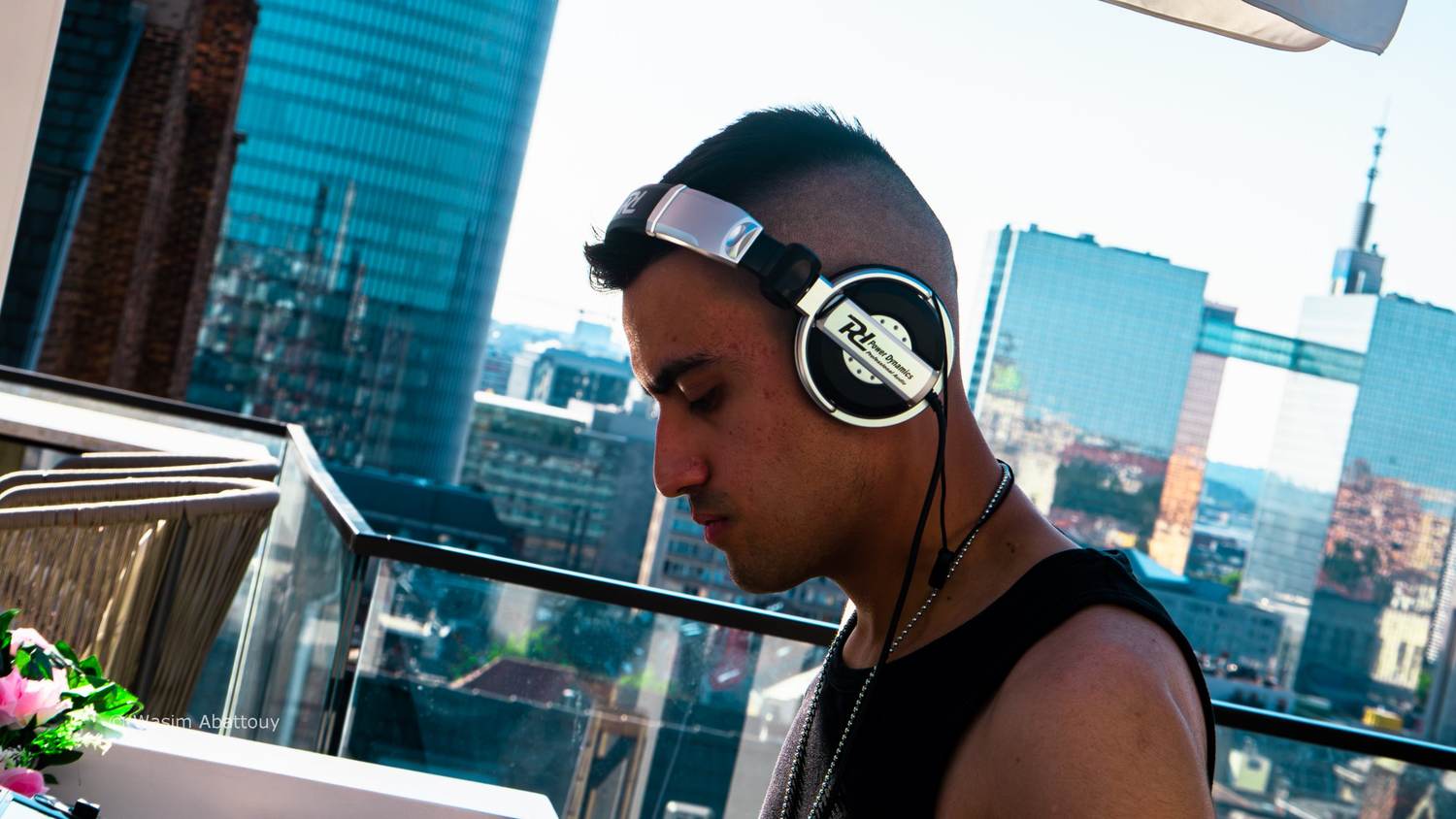 DJ in headphones in profile on a rooftop terrace, with the Brussels skyline behind