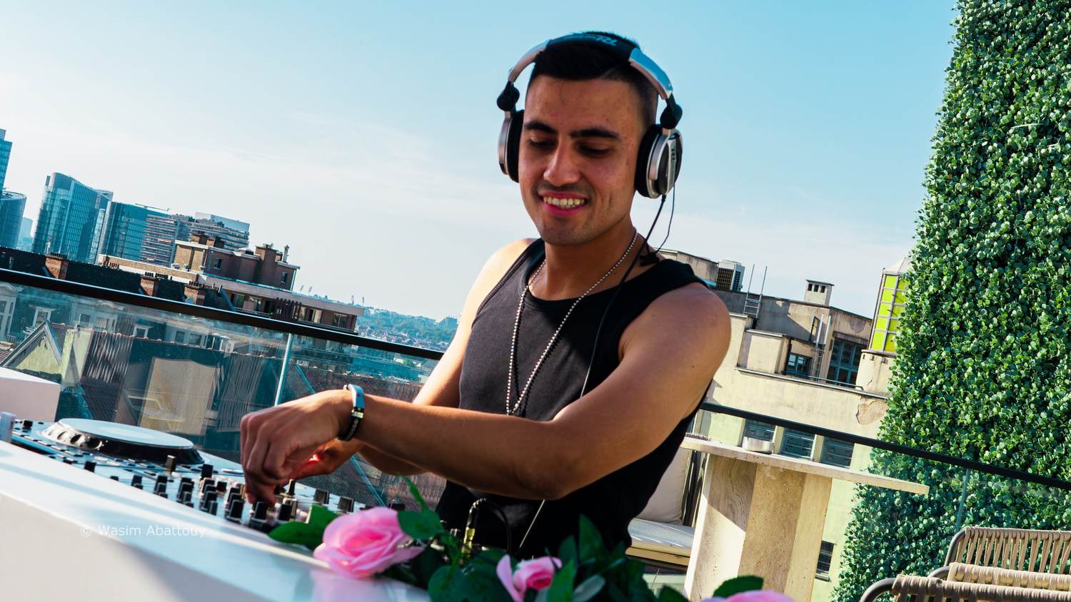 Smiling DJ mixing on a rooftop terrace, pink roses on the booth