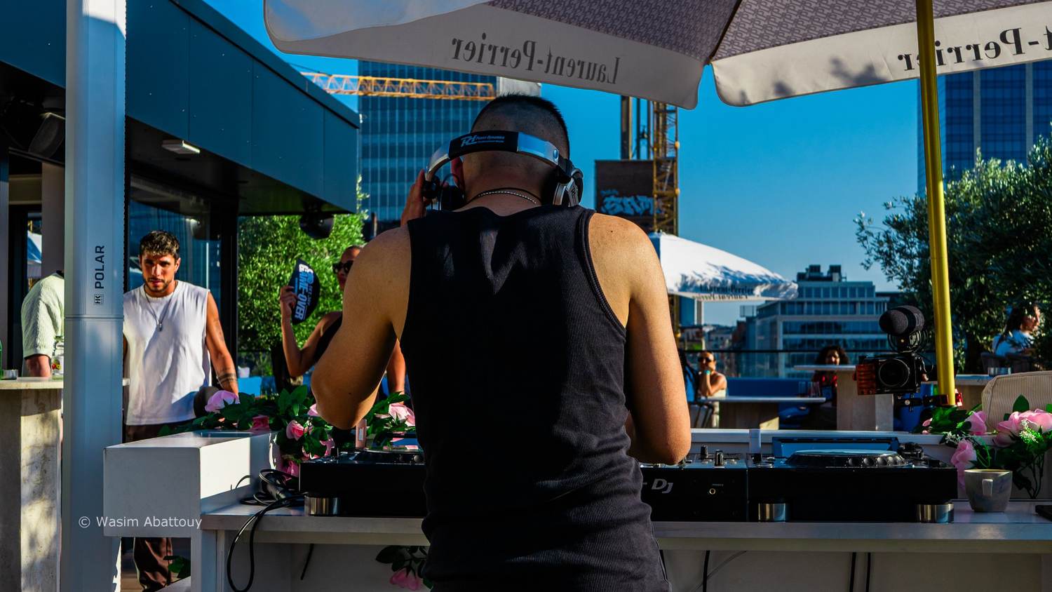 DJ seen from behind at the decks, guests and a camera with a microphone in the background