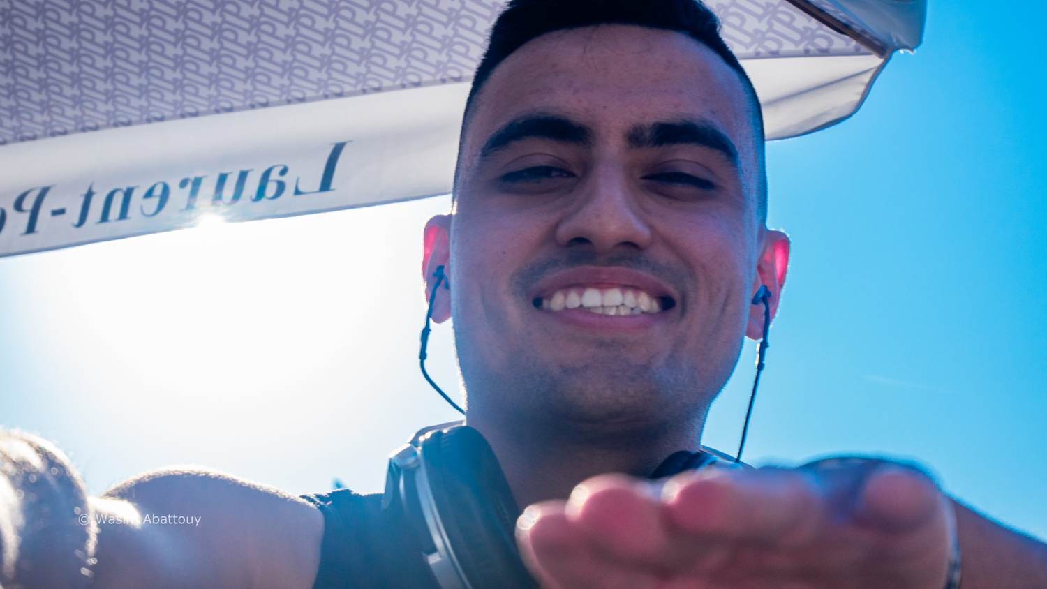 Low-angle close-up of the DJ smiling, with a hand reaching toward the camera