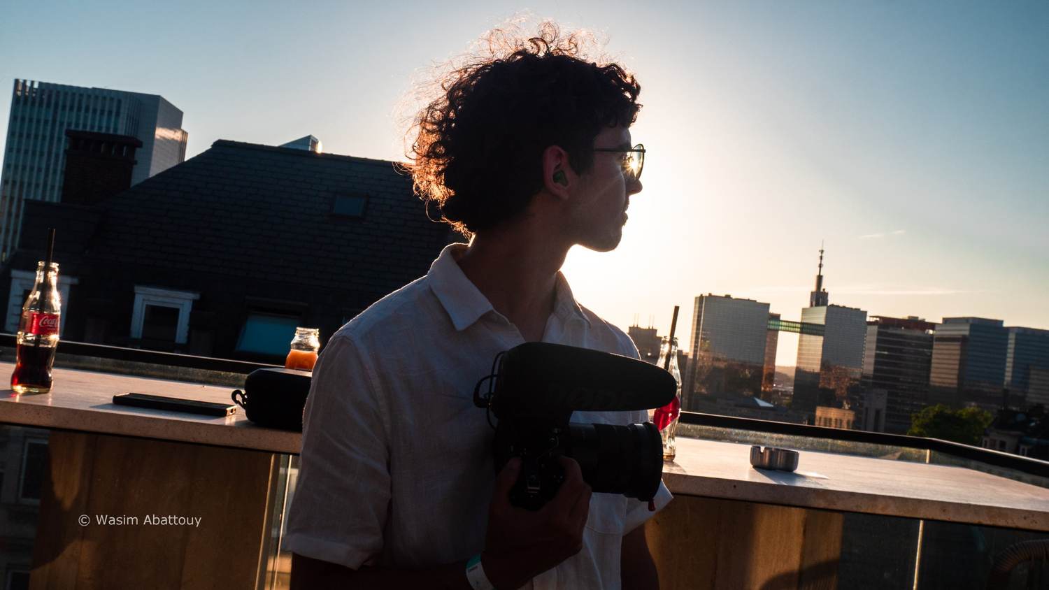 Silhouette of a camera operator holding a camera with a microphone, backlit by the setting sun