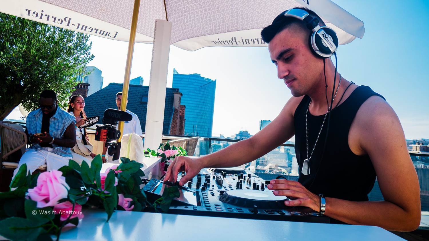 DJ mixing at a controller with pink roses in the foreground, guests behind him