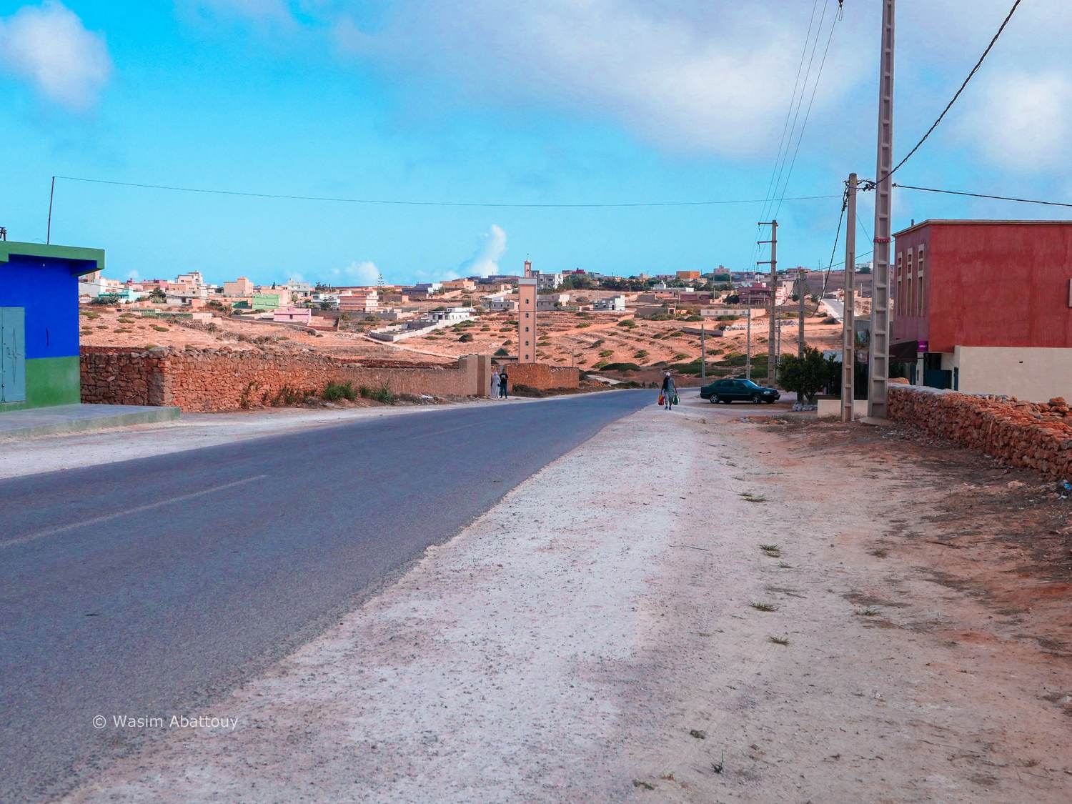 A village road leading to a minaret, with colourful houses and power poles