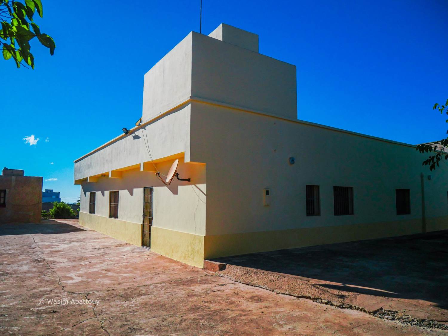 A white and yellow building with a satellite dish under a blue sky
